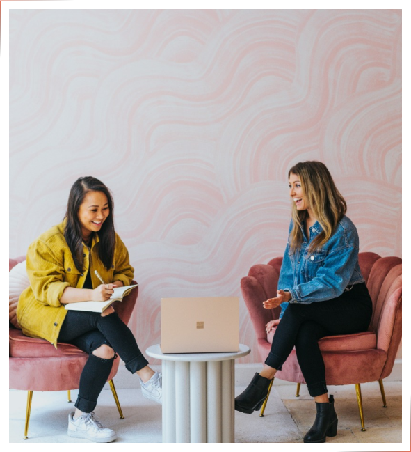 Two women sitting in pink chairs, Doing therapy session while NuIQ is on their laptop writing therapy notes.